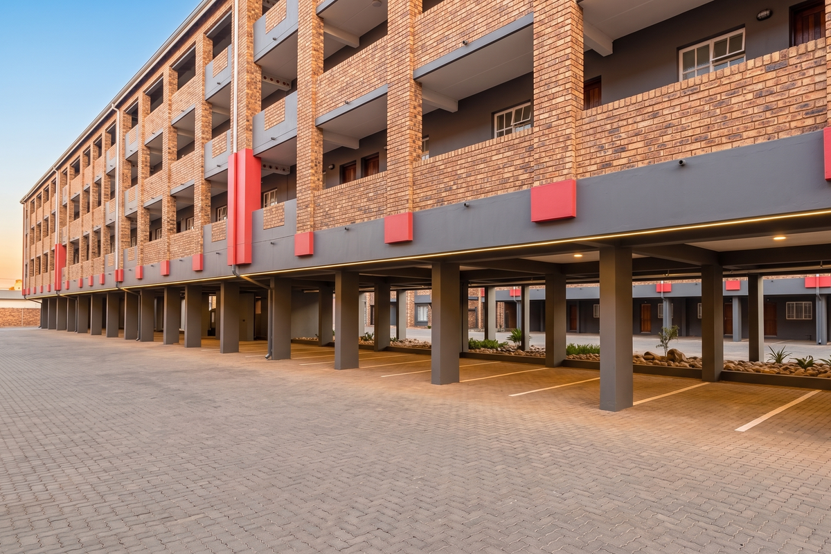 A modern apartment building exterior featuring a brick facade, covered ground-level parking, and paved driveway access.