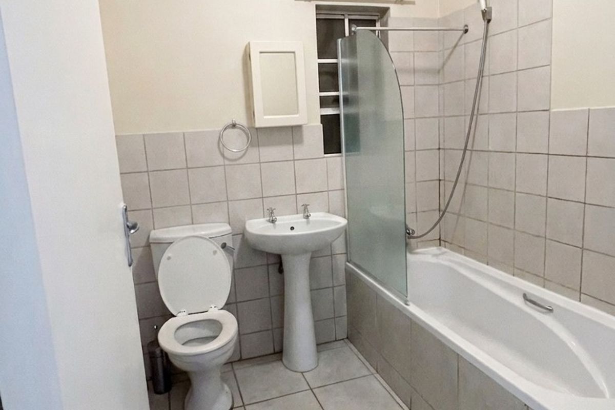 A functional bathroom featuring a pedestal basin, toilet, and a bathtub with a glass shower screen and tiled finishes.