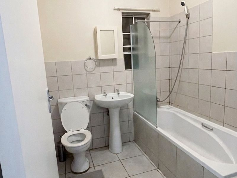 A functional bathroom featuring a pedestal basin, toilet, and a bathtub with a glass shower screen and tiled finishes.