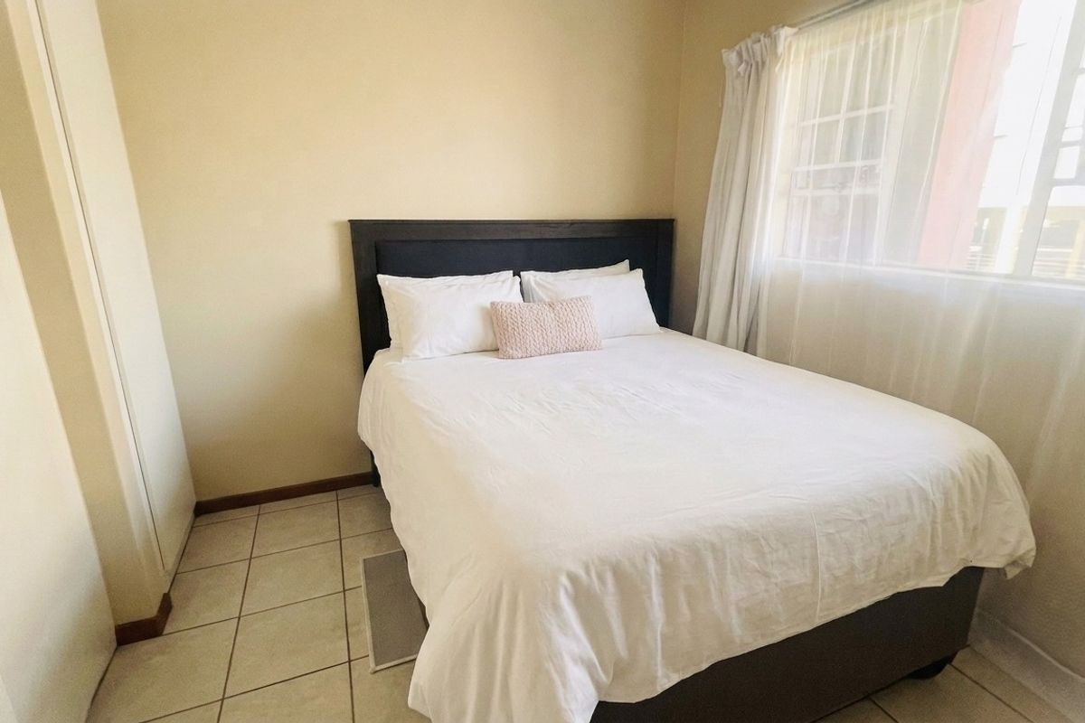 A functional bedroom featuring tiled flooring, a built-in cupboard, and a window with security bars, providing a simple and practical living space.