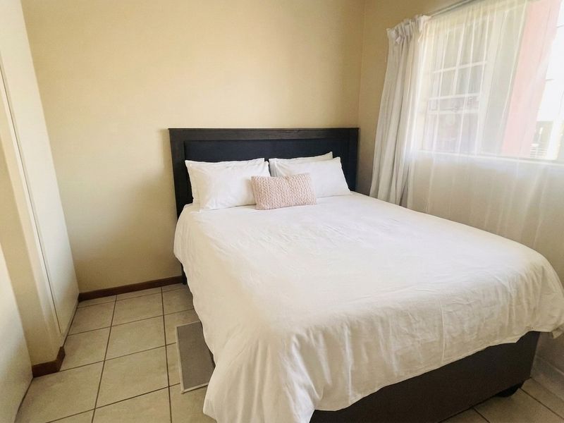 A functional bedroom featuring tiled flooring, a built-in cupboard, and a window with security bars, providing a simple and practical living space.