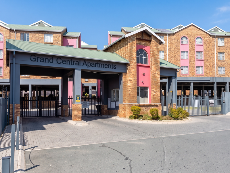 Front entrance and security gate access to the Grand Central Apartments complex, featuring brick facade architecture and paved driveway.