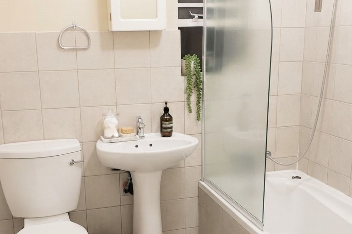 A functional bathroom featuring a pedestal basin, toilet, and a bathtub with a glass shower screen and tiled finishes.