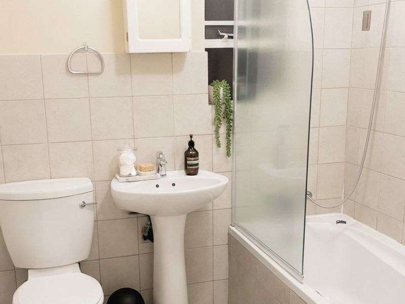 A functional bathroom featuring a pedestal basin, toilet, and a bathtub with a glass shower screen and tiled finishes.