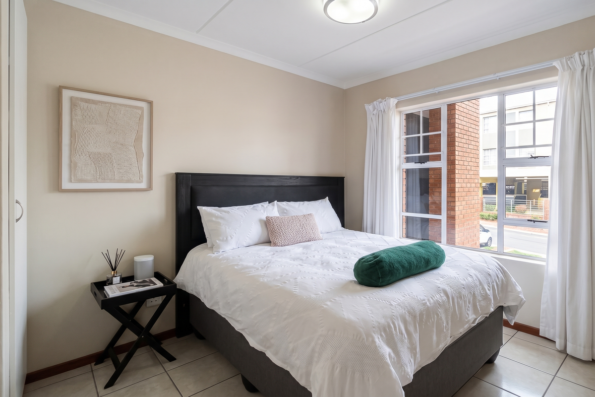 A well-maintained bedroom featuring tiled flooring, a built-in wardrobe, and large windows that provide natural light.