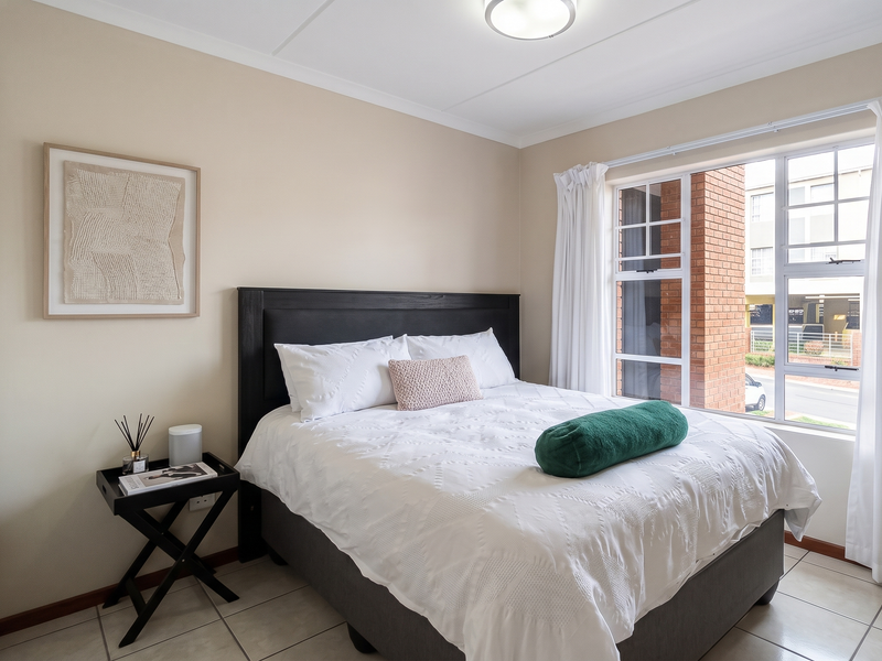 A well-maintained bedroom featuring tiled flooring, a built-in wardrobe, and large windows that provide natural light.