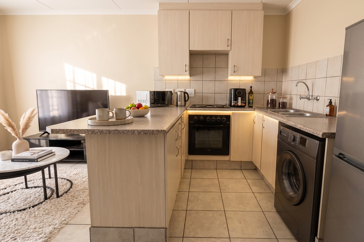Open-plan kitchen featuring light wood cabinetry, laminate countertops, integrated appliances, and tiled flooring, seamlessly connecting to the living area.