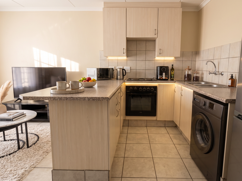 Open-plan kitchen featuring light wood cabinetry, laminate countertops, integrated appliances, and tiled flooring, seamlessly connecting to the living area.