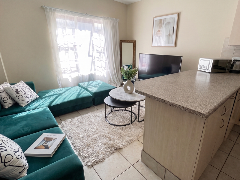 Open-plan living area featuring a compact kitchen with laminate cabinetry, tiled flooring, and a seamless flow into the lounge space.