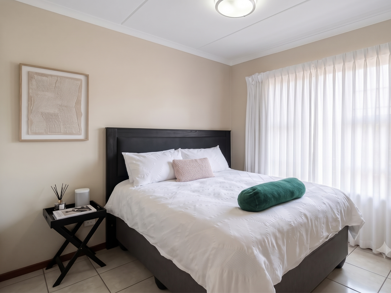 A well-maintained bedroom featuring neutral wall tones, tiled flooring, and a built-in wardrobe, complemented by natural light through floor-to-ceiling curtains.