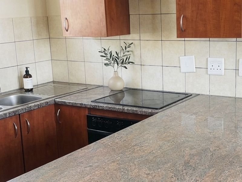 A functional kitchen featuring wood-tone laminate cabinetry, granite-look laminate countertops, a ceramic tile backsplash, and integrated electric cooking appliances.