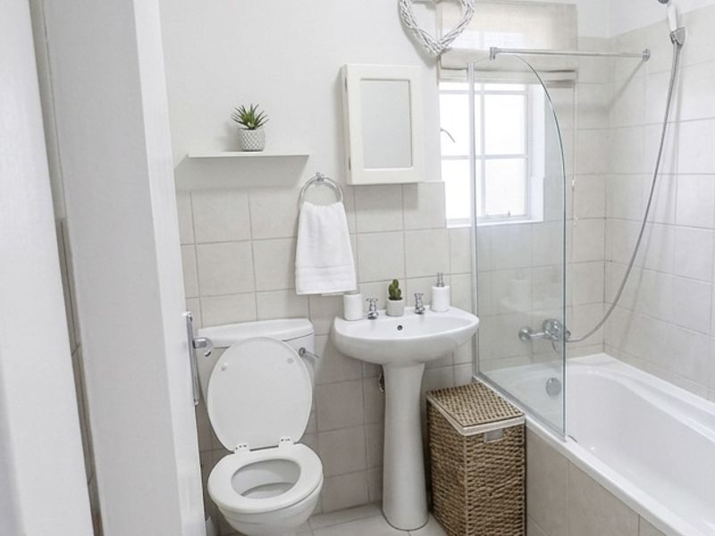 A clean and functional bathroom featuring a pedestal basin, toilet, and a bathtub with a glass shower screen and tiled finishes.