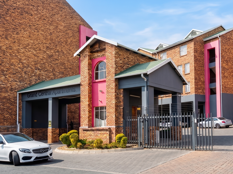 Front entrance view of Grand Central Apartments featuring face brick architecture, secure gated access, and paved driveway.