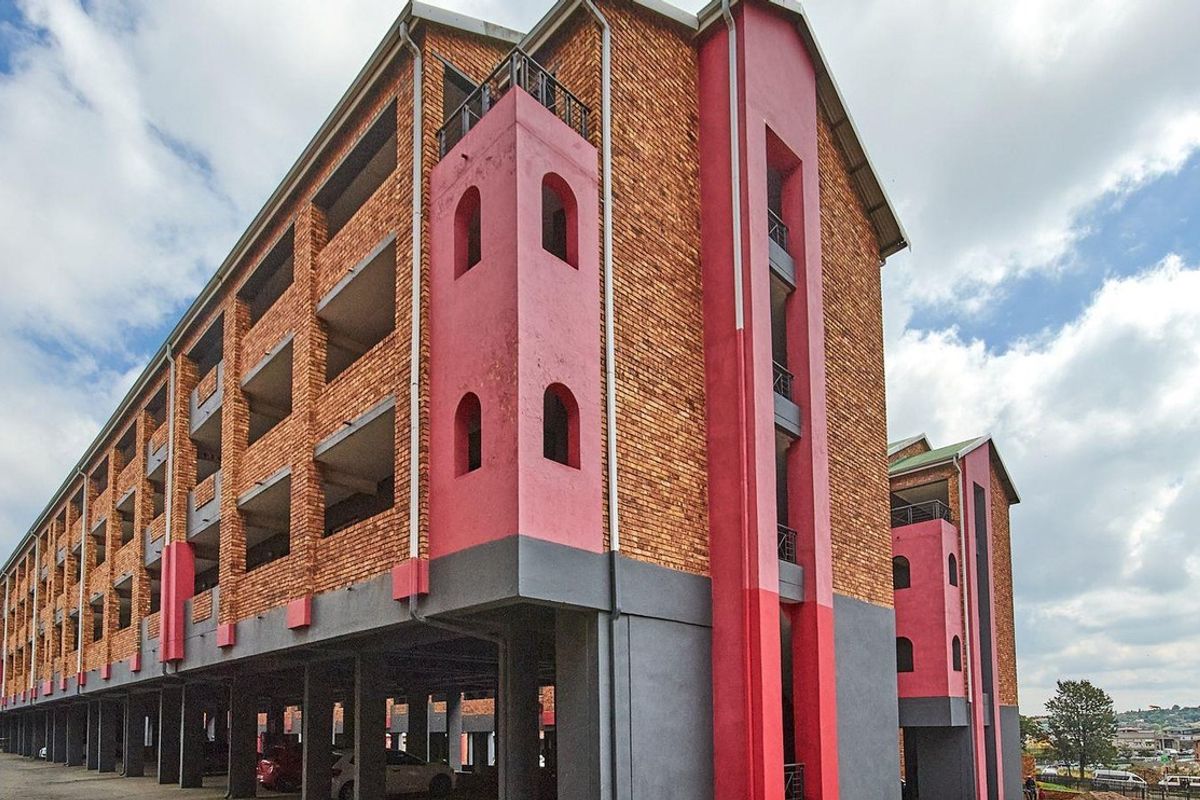 Exterior view of a multi-story apartment building featuring exposed brickwork, pink accent pillars, and a ground-level covered parking area.