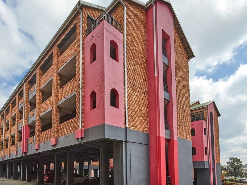 Exterior view of a multi-story apartment building featuring exposed brickwork, pink accent pillars, and a ground-level covered parking area.