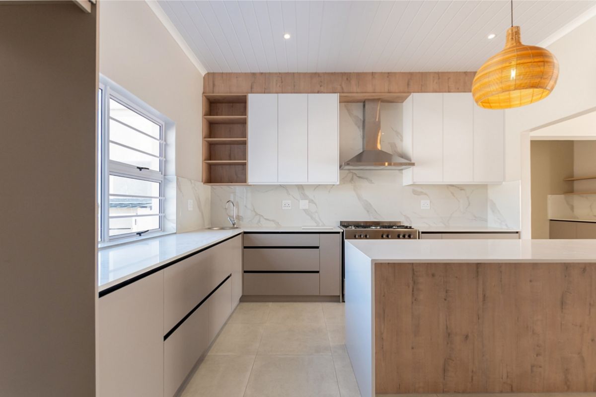 Modern kitchen featuring sleek handleless cabinetry, stone countertops, marble-look splashback, and a central island, complemented by a stylish tongue and groove ceiling.