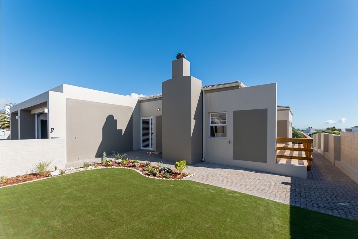 Rear view of the property featuring a paved patio, a raised timber deck, a central chimney, and a well-maintained landscaped garden.