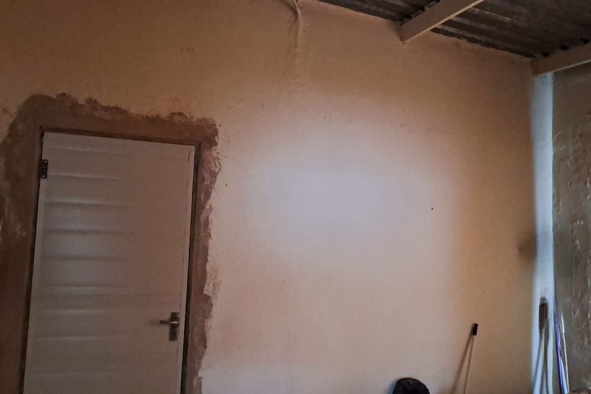 An unfinished bedroom interior featuring exposed ceiling beams and rough plasterwork around the door frame, requiring cosmetic renovation and finishing.