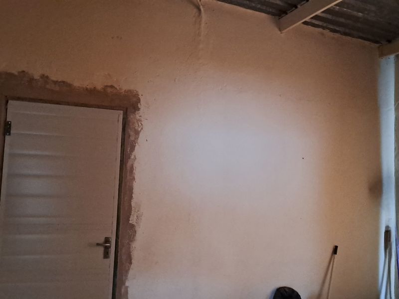 An unfinished bedroom interior featuring exposed ceiling beams and rough plasterwork around the door frame, requiring cosmetic renovation and finishing.