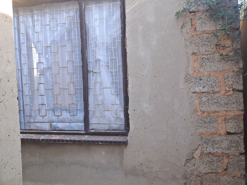 Exterior view of a side passage showing weathered plaster walls, exposed brickwork, and a window with security bars.
