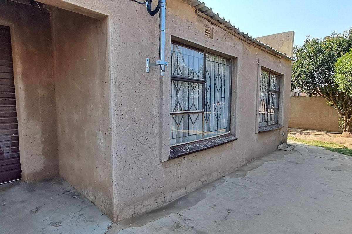 Rear exterior view of the property featuring a concrete patio, roller shutter garage door, and security bars on the windows.