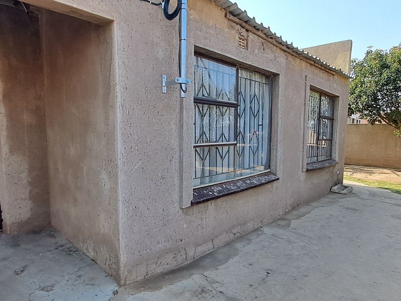 Rear exterior view of the property featuring a concrete patio, roller shutter garage door, and security bars on the windows.