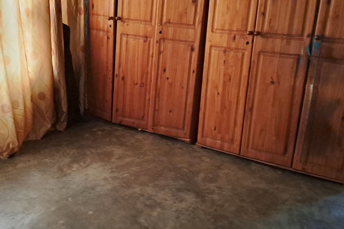 A bedroom featuring built-in wooden wardrobes and concrete flooring, requiring cosmetic updates to improve the overall finish and appeal.