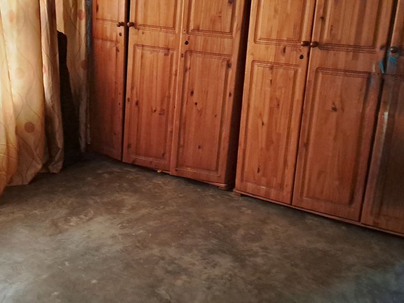 A bedroom featuring built-in wooden wardrobes and concrete flooring, requiring cosmetic updates to improve the overall finish and appeal.