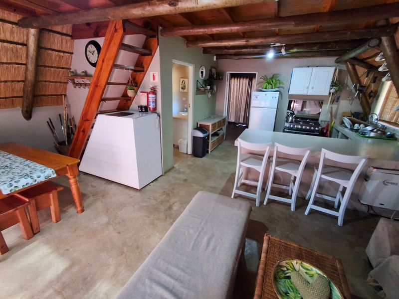 Open-plan living and kitchen area featuring exposed timber beams, a central staircase, concrete flooring, and a functional kitchen layout with a breakfast bar.