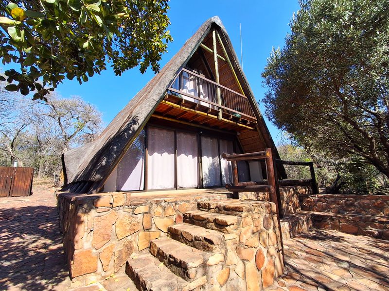 A-frame house featuring a traditional thatched roof, stone-clad base, and a private timber balcony overlooking the surrounding natural landscape.