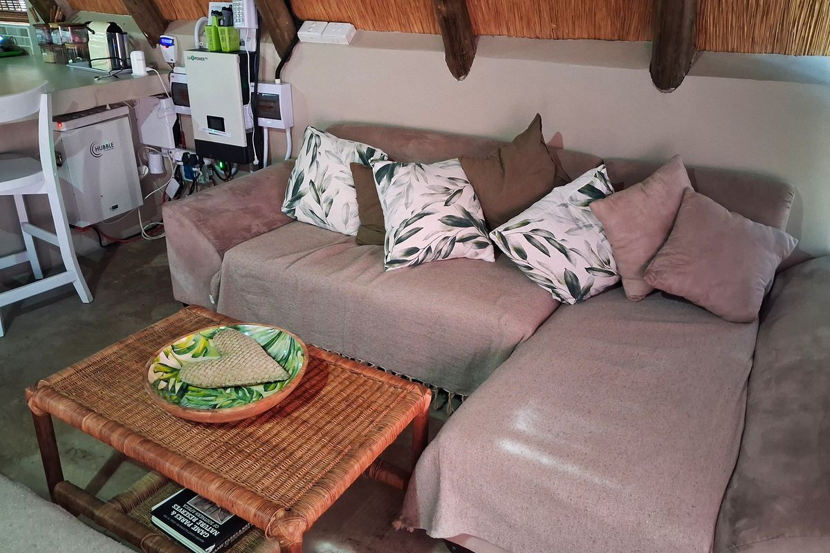 Cozy living area featuring a unique thatched roof with exposed timber rafters and a wall-mounted solar inverter system.