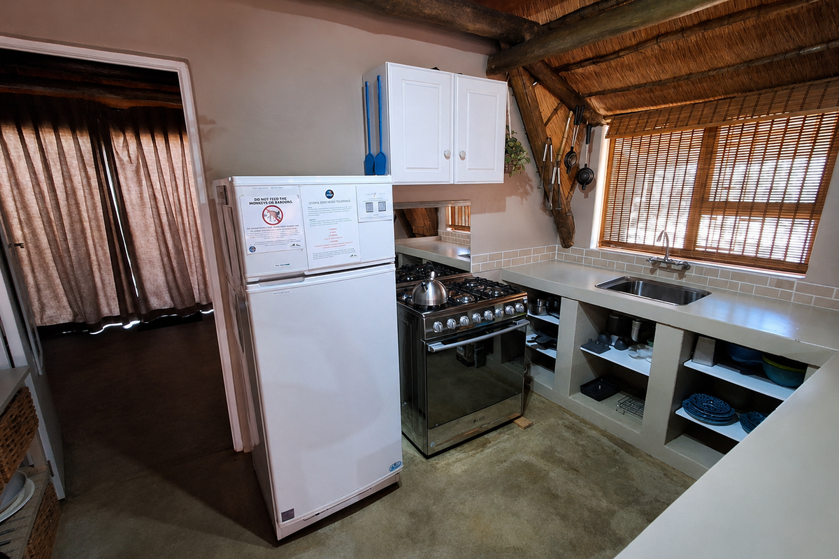 A rustic kitchen featuring a stainless steel gas stove, concrete countertops with open shelving, and a distinctive thatched ceiling with exposed timber beams.