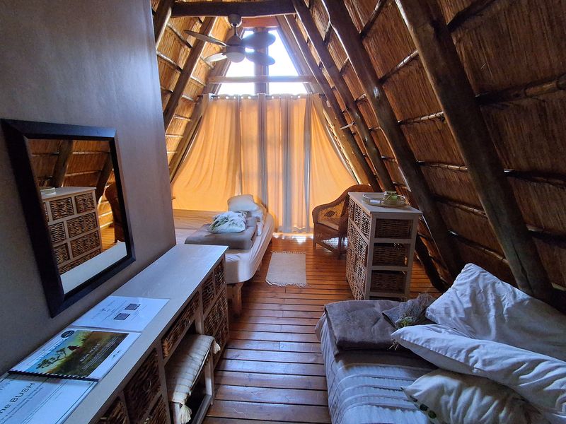 A cozy loft-style bedroom featuring a high-pitched thatched roof with exposed timber rafters, timber flooring, and a ceiling fan.