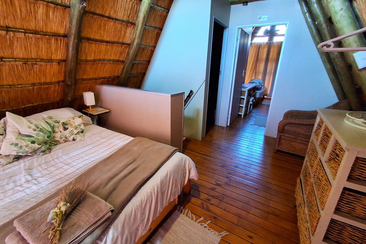 A rustic bedroom featuring exposed timber rafters, a thatched roof ceiling, and warm timber flooring, creating a cozy, cabin-style atmosphere.