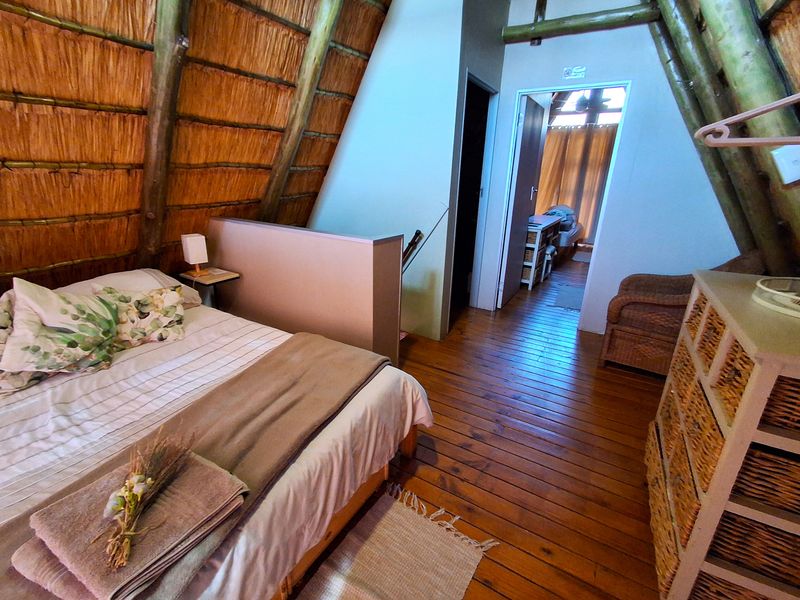 A rustic bedroom featuring exposed timber rafters, a thatched roof ceiling, and warm timber flooring, creating a cozy, cabin-style atmosphere.