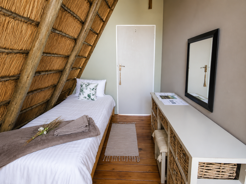 A cozy bedroom featuring a unique slanted thatched roof, timber flooring, and a neutral color palette.