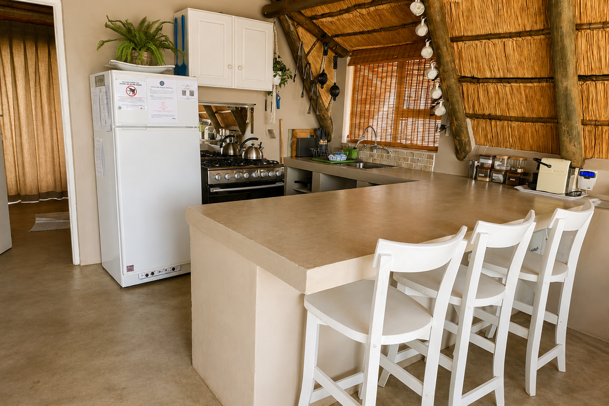 Rustic kitchen featuring a thatched roof, exposed timber rafters, concrete countertops, and a gas stove, offering a unique, character-filled cooking and dining space.