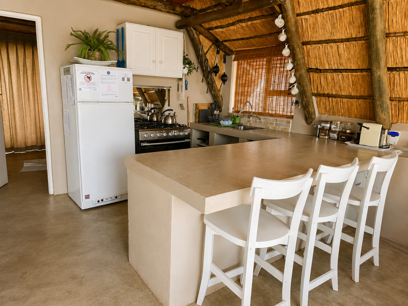 Rustic kitchen featuring a thatched roof, exposed timber rafters, concrete countertops, and a gas stove, offering a unique, character-filled cooking and dining space.