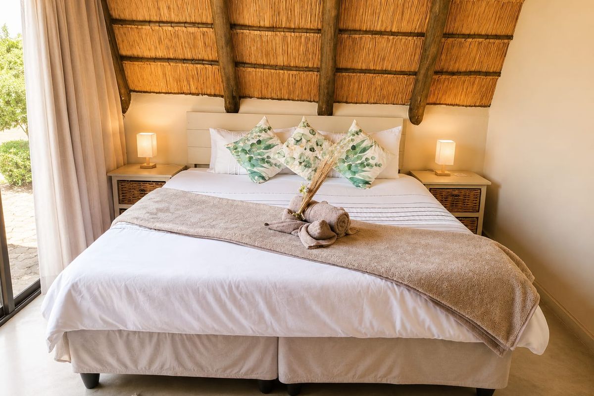 A cozy bedroom featuring a unique thatched roof with exposed timber rafters and a sliding glass door providing natural light and garden access.