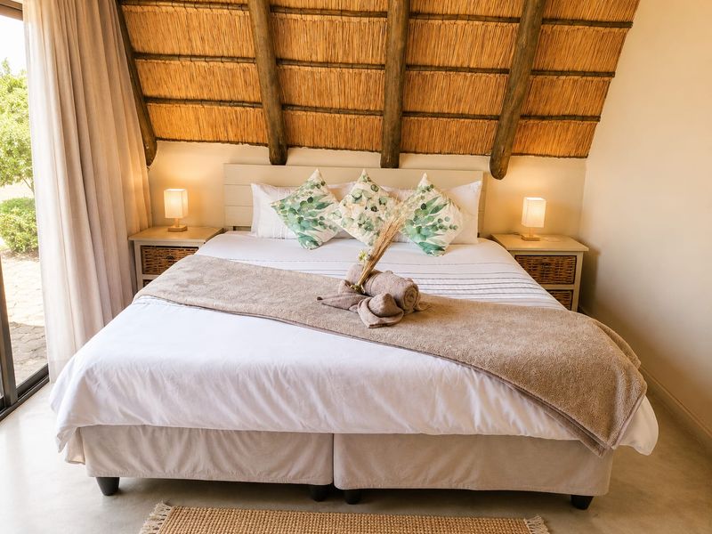 A cozy bedroom featuring a unique thatched roof with exposed timber rafters and a sliding glass door providing natural light and garden access.