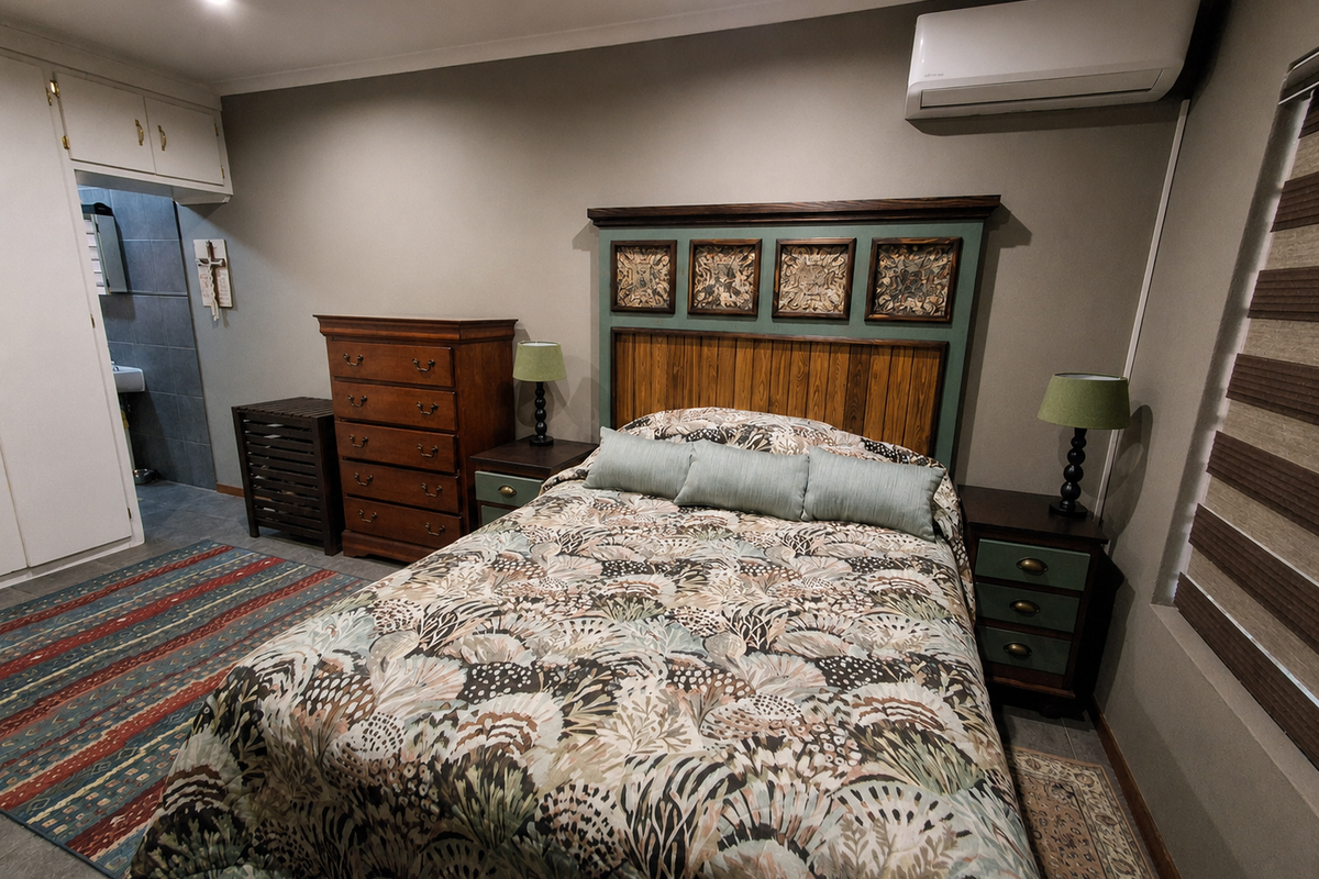 A bedroom featuring built-in cupboards, a wall-mounted split-system air conditioner, and roller blinds, with an adjoining en-suite bathroom area.