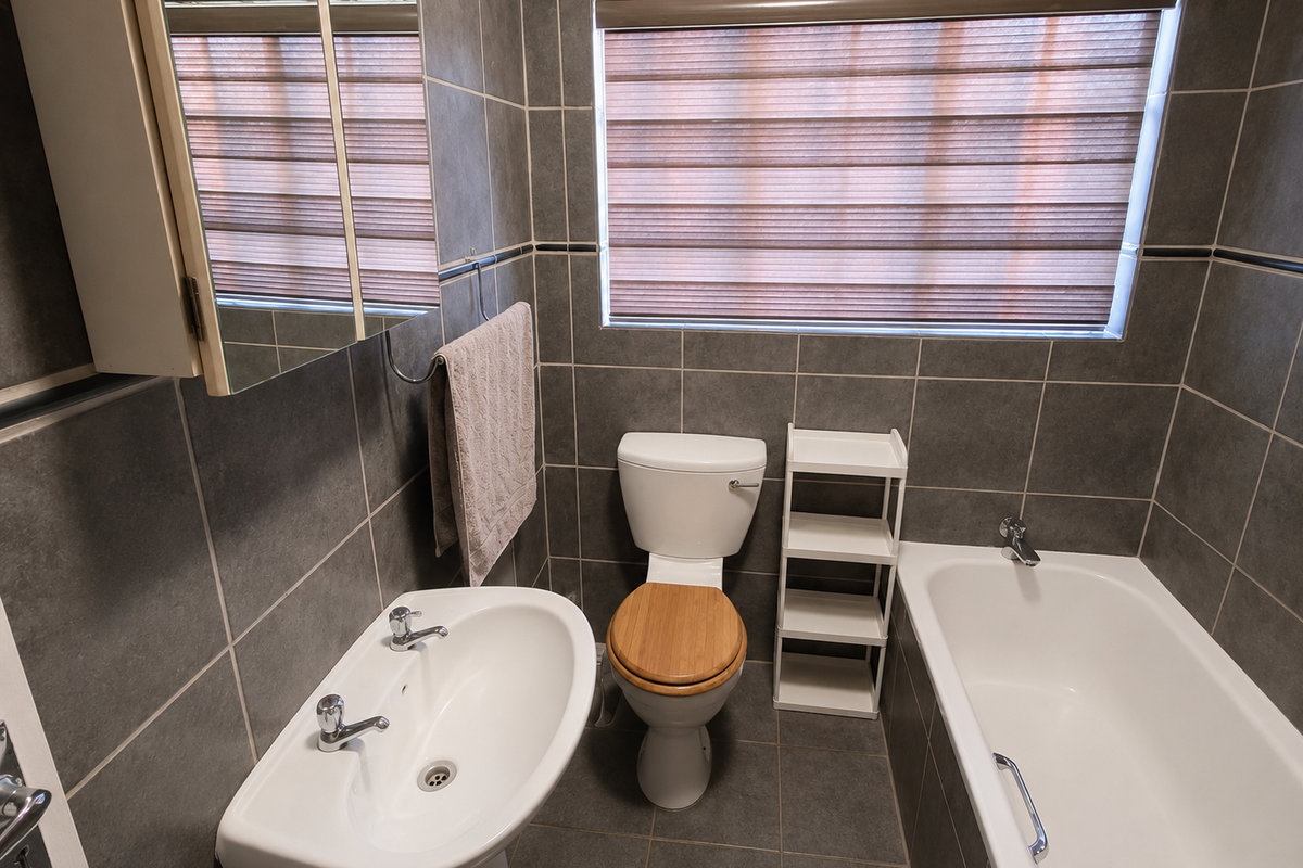 A clean, modern bathroom featuring grey wall and floor tiles, a pedestal basin, a bathtub, and a built-in medicine cabinet.