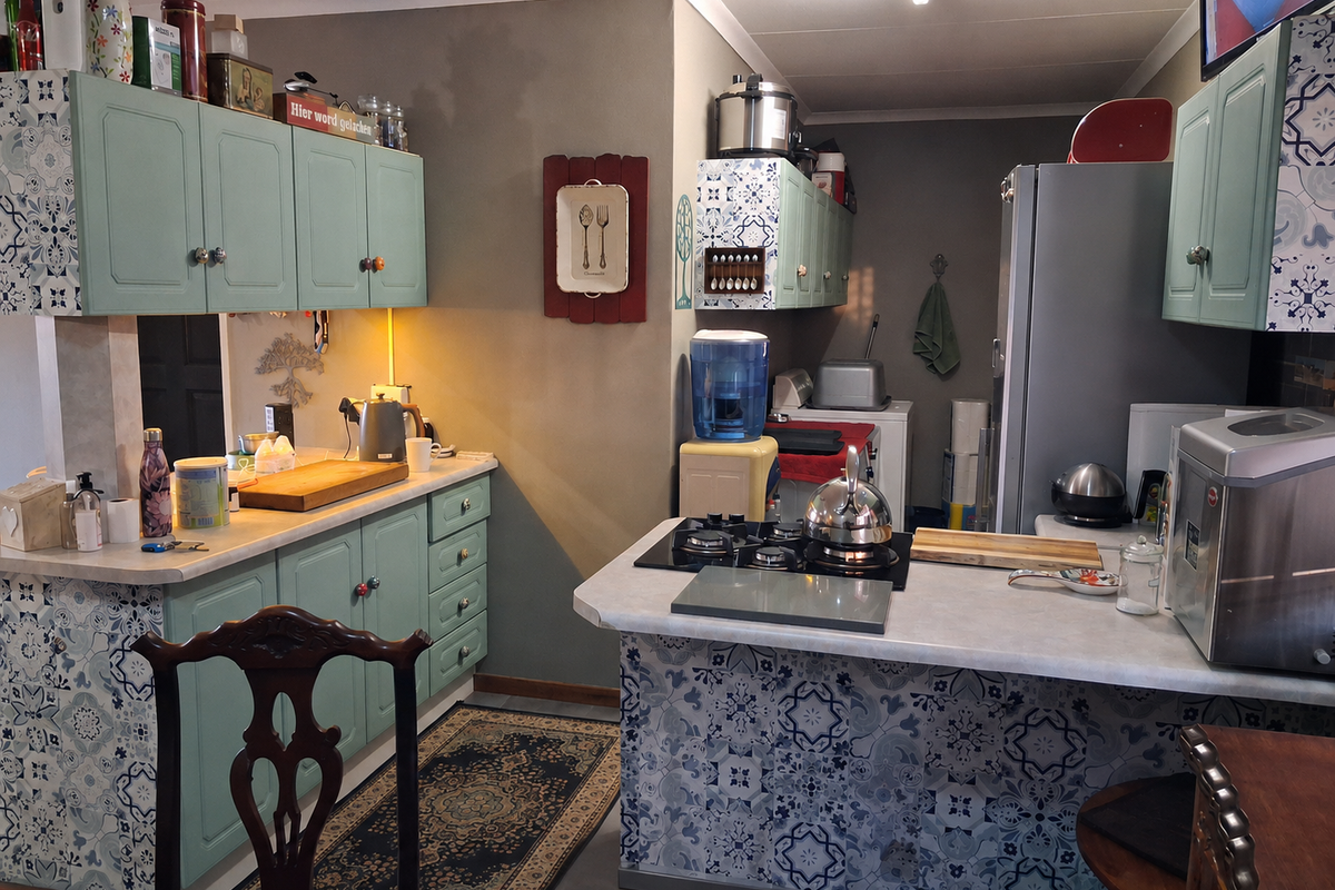 A functional kitchen featuring light green cabinetry, patterned tile accents, and a gas hob set into a peninsula countertop.