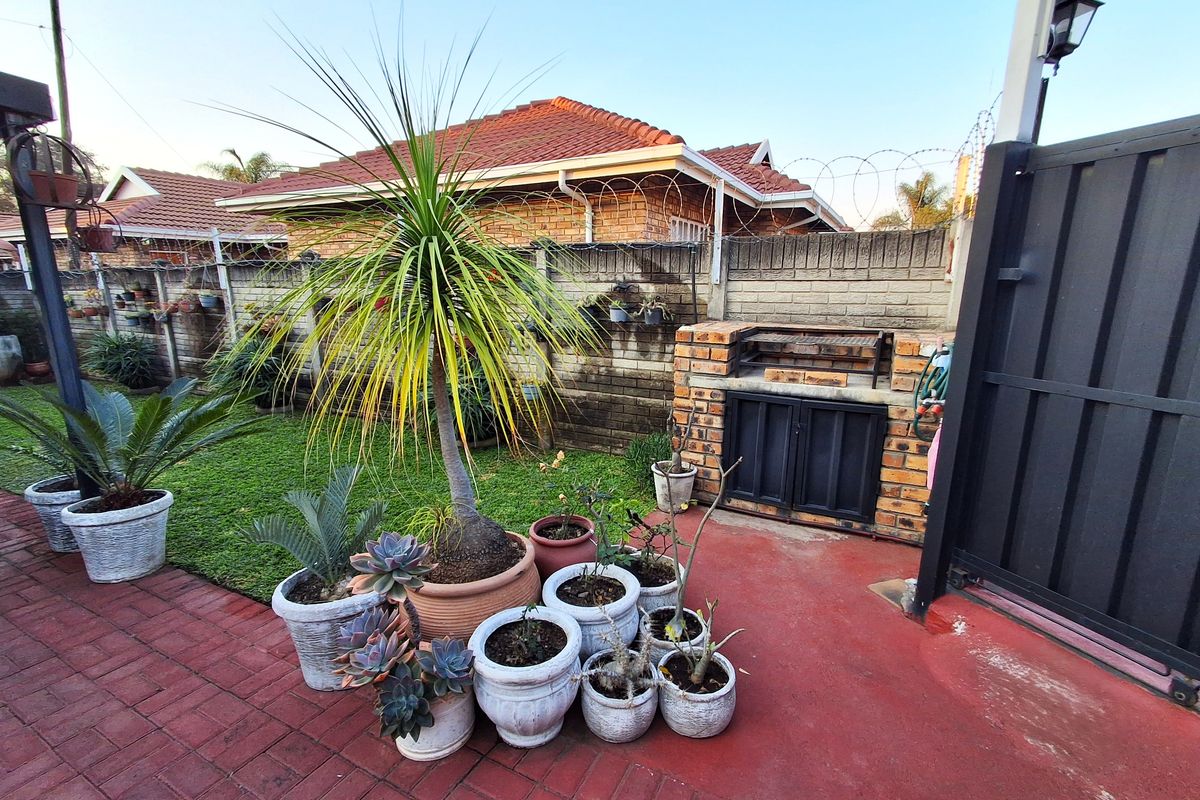 Rear garden area featuring a paved patio, a built-in brick braai, and perimeter walling with security fencing.