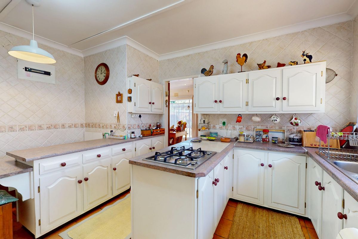 A functional kitchen featuring white cabinetry, a gas cooktop, double bowl sink, and tiled backsplash, offering a classic layout with potential for modern updates.