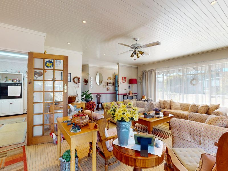Open-plan living area featuring a timber-paneled ceiling, ceiling fan, and an adjacent kitchen with built-in cabinetry and appliances.
