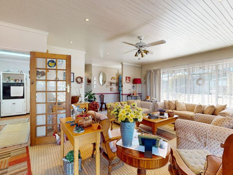 Open-plan living area featuring a timber-paneled ceiling, ceiling fan, and an adjacent kitchen with built-in cabinetry and appliances.
