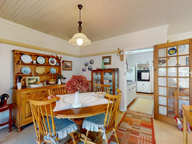 A traditional dining room featuring a tongue and groove ceiling, picture rails, and a classic pendant light, with direct access to the kitchen.