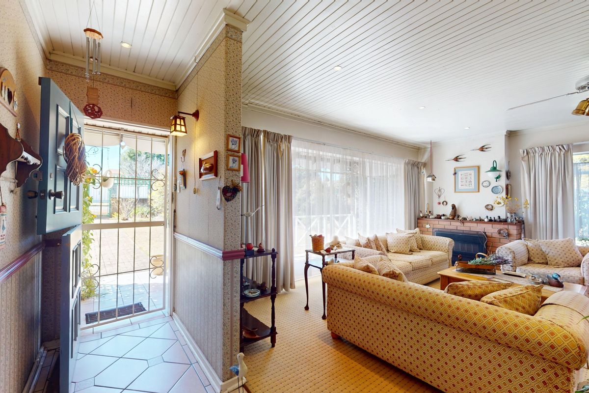 A living room featuring a brick fireplace, timber panelled ceiling, and direct access to the exterior through a security screen door.