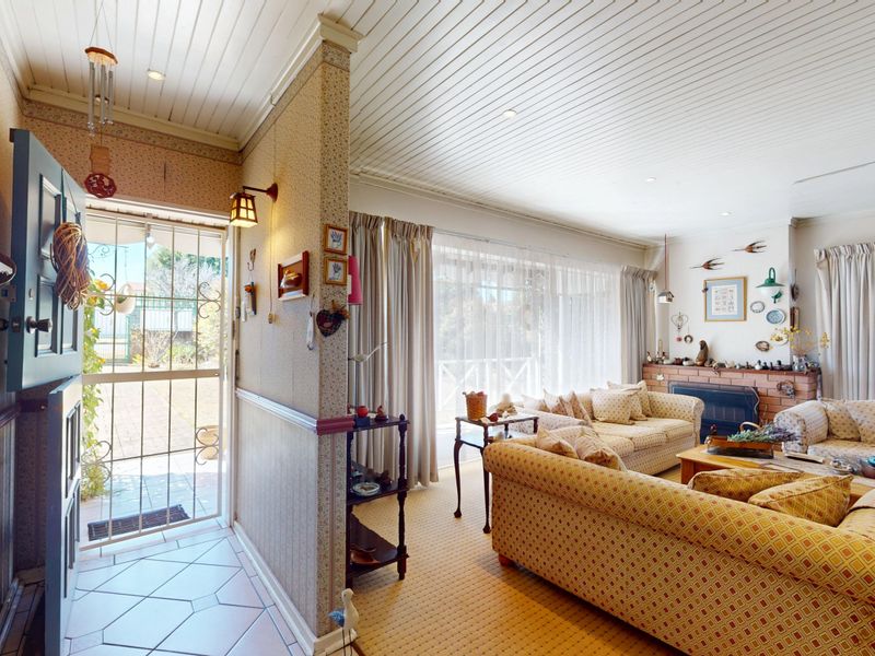A living room featuring a brick fireplace, timber panelled ceiling, and direct access to the exterior through a security screen door.